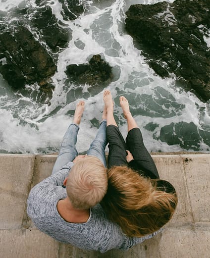 man and woman sitting on cliff near body of water